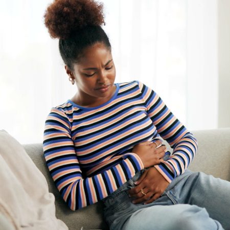 Cramps, pain and woman in lounge, home and reaction to food poisoning, indigestion and uncomfortabl.